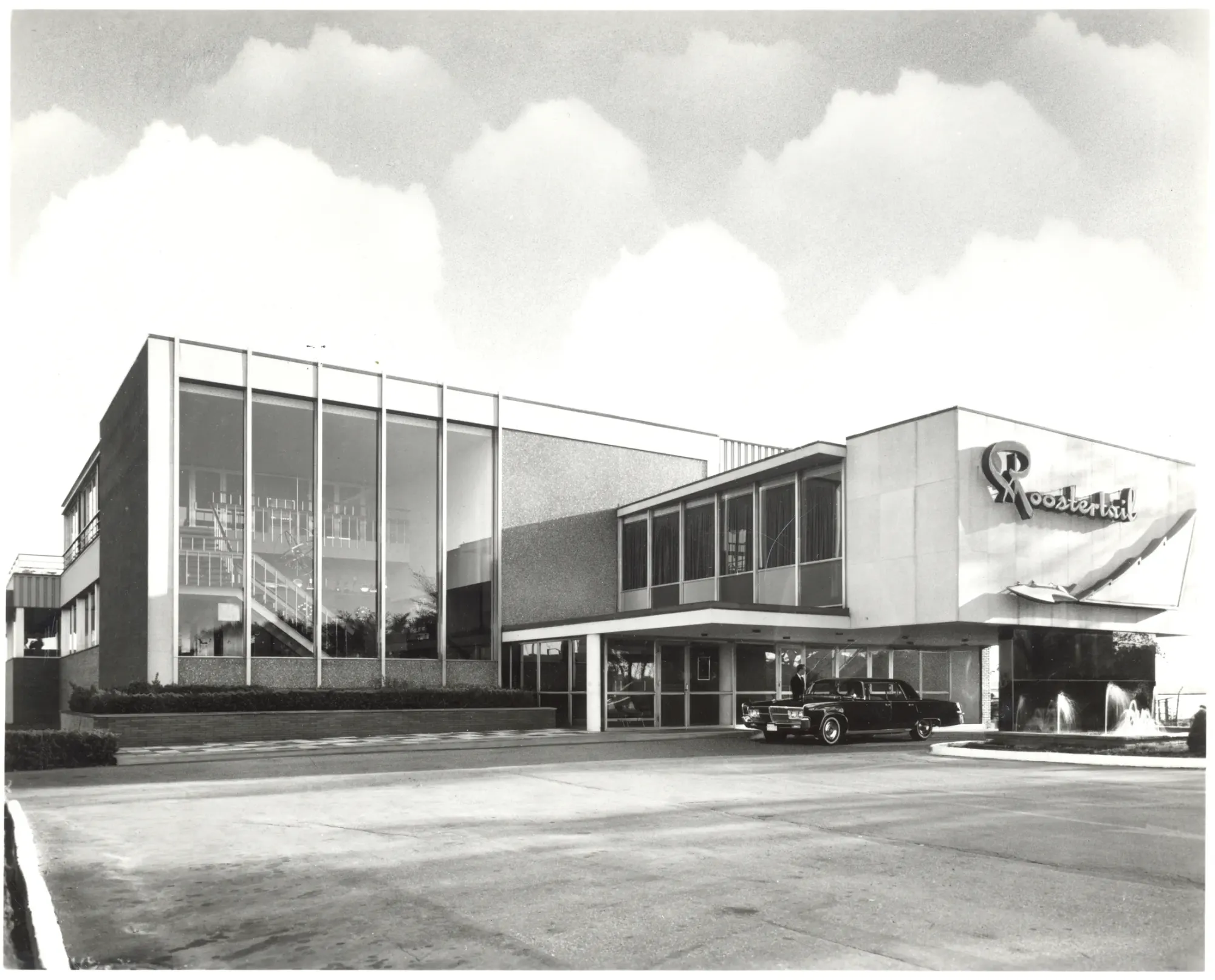 The Roostertail in daylight, the script sign on the wall and a black car waiting under the entrance canopy