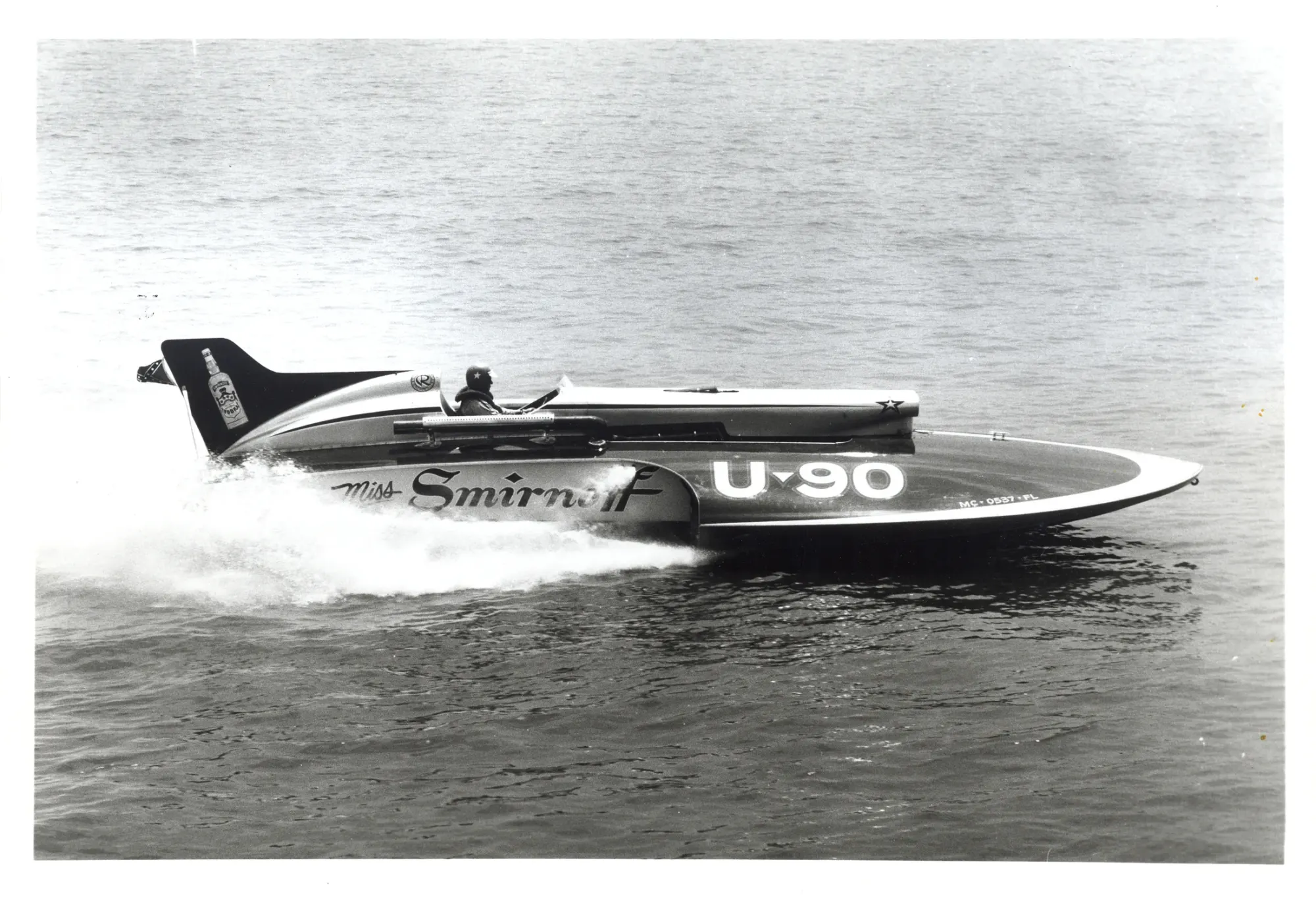 The unlimited hydroplane Miss Smirnoff, hull number U-90, running flat out on open water with white spray thrown up behind its stern and the driver low in an open cockpit.