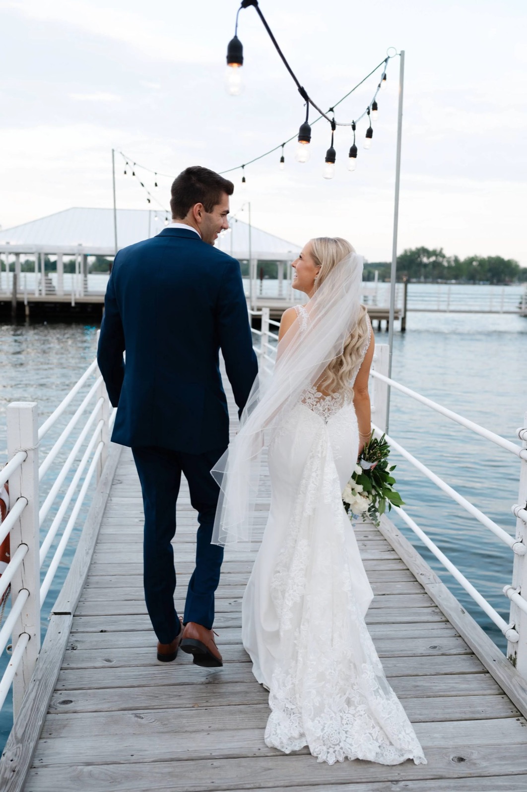 Couple walking the dock under string lights at twilight